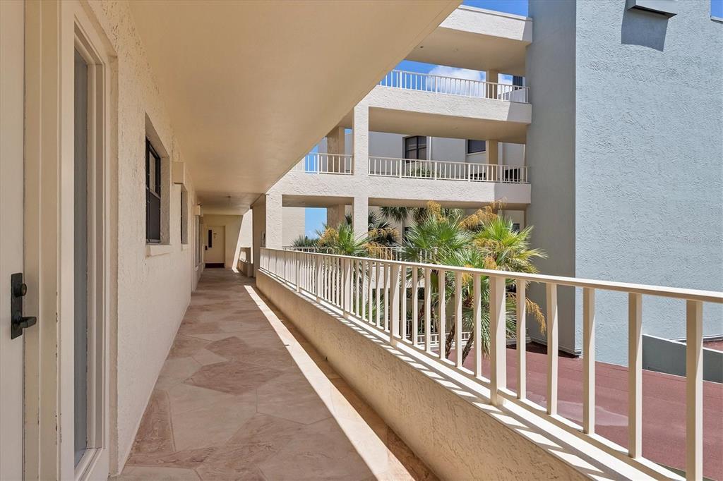 An outdoor walkway with tiled flooring and a white metal railing overlooks a courtyard — 5740 MIDNIGHT PASS ROAD UNIT 303F, SARASOTA, FL