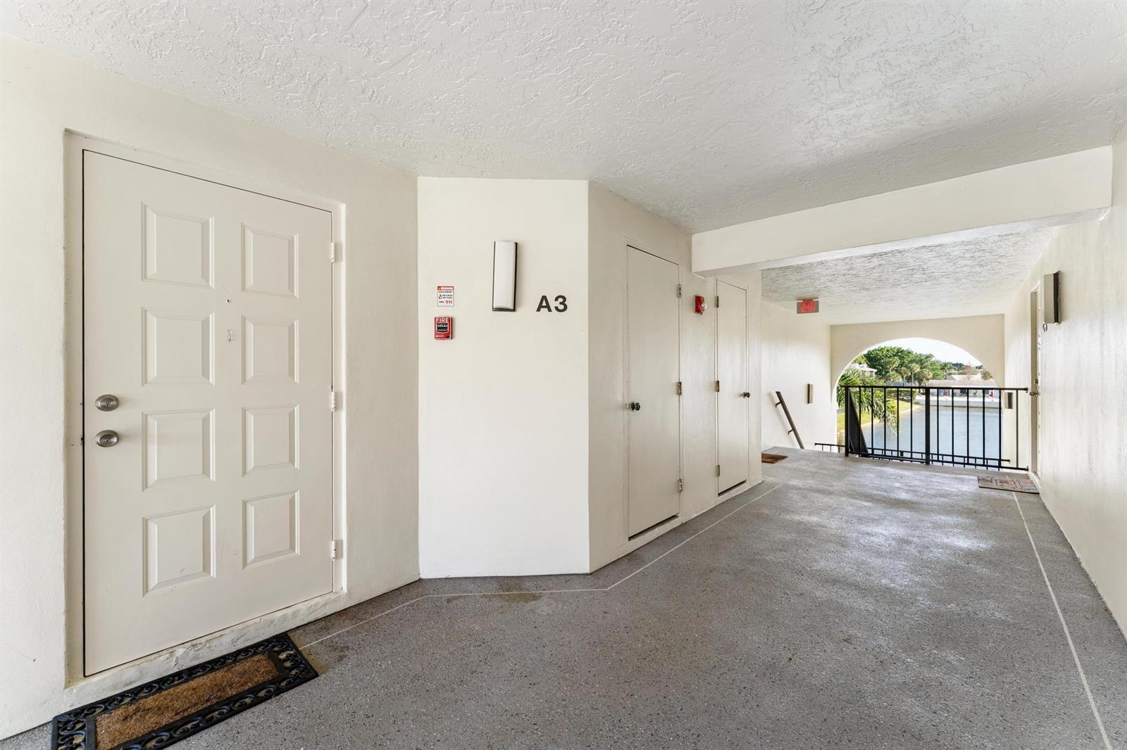 An outdoor apartment hallway features a white door labeled A3, concrete flooring, and a balcony — 1108 Green Pine Boulevard # A3, West Palm Beach FL 33409, WEST PALM BEACH, FL