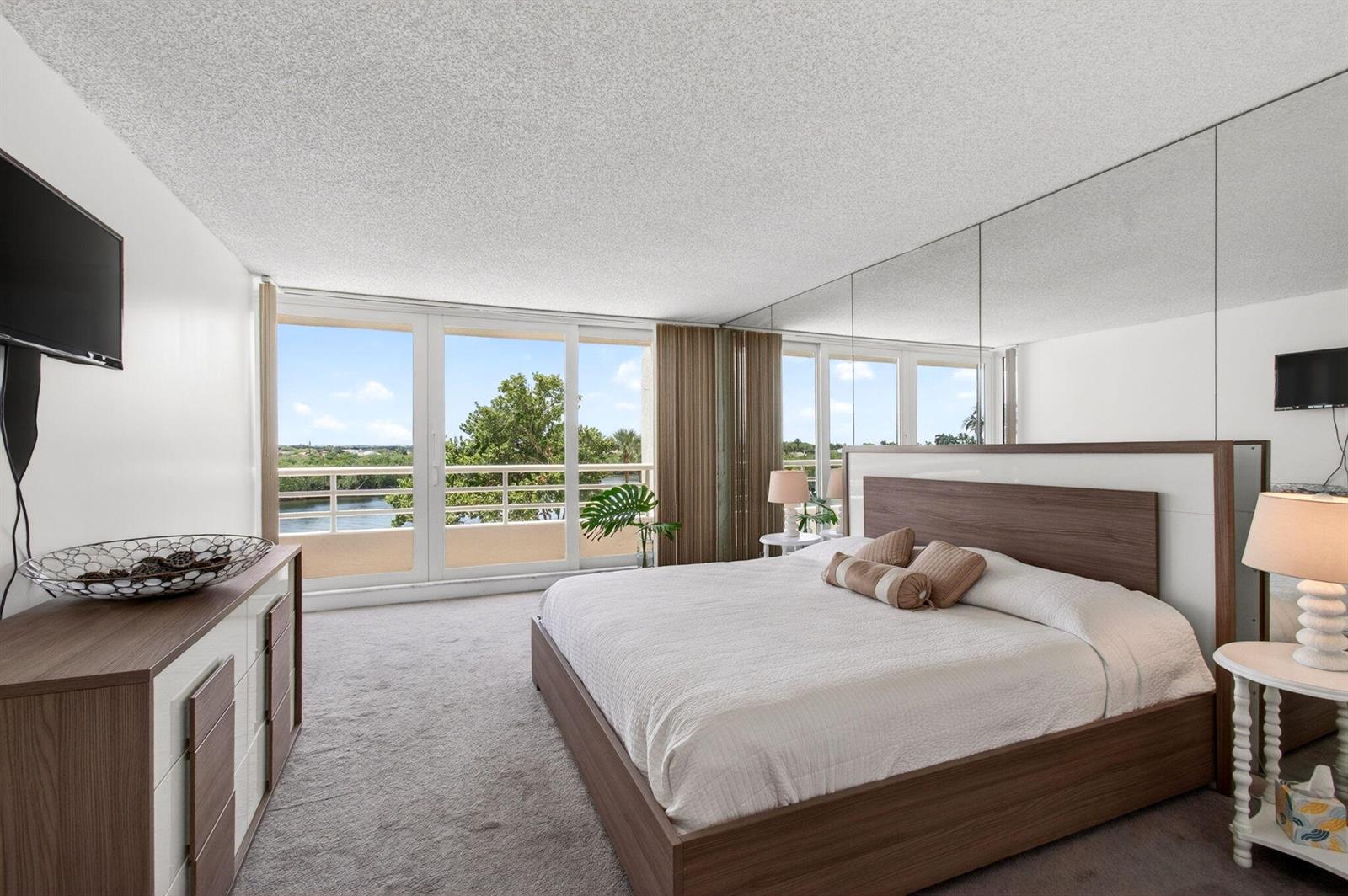 A bedroom with a king bed, mirrored wall, and a balcony overlooking a waterway — 4201 N Ocean Boulevard # 307, Boca Raton FL 33431, BOCA RATON, FL