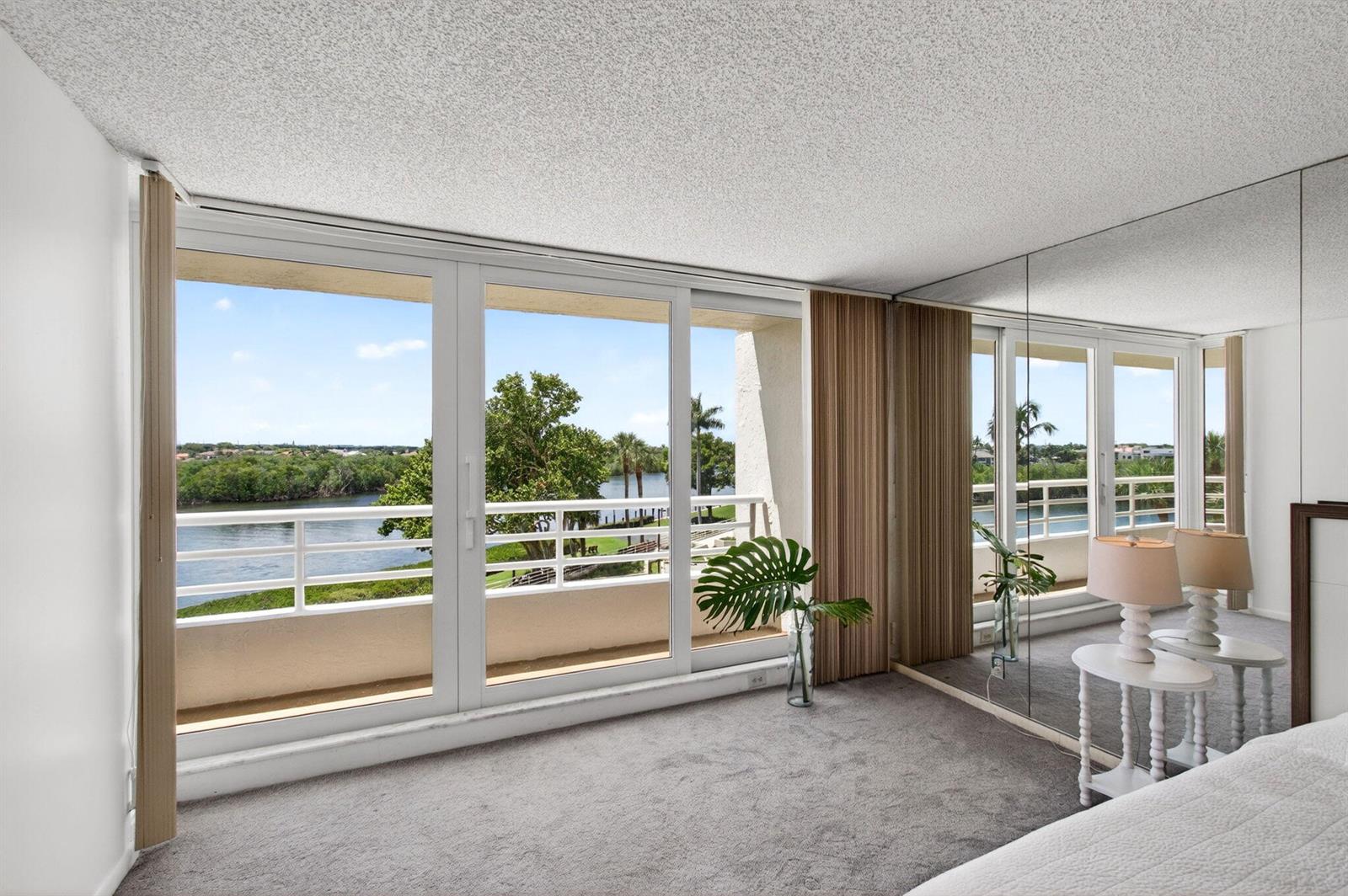 A bedroom with gray carpet, mirrored walls, and sliding glass doors opening to a water view — 4201 N Ocean Boulevard # 307, Boca Raton FL 33431, BOCA RATON, FL