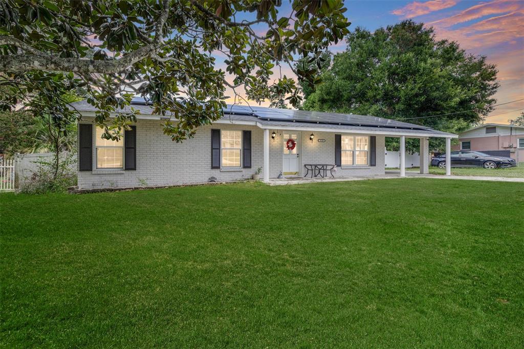 A single-story brick house with solar panels and a front porch sits behind a lawn — 37237 NICOLE AVENUE, ZEPHYRHILLS, FL