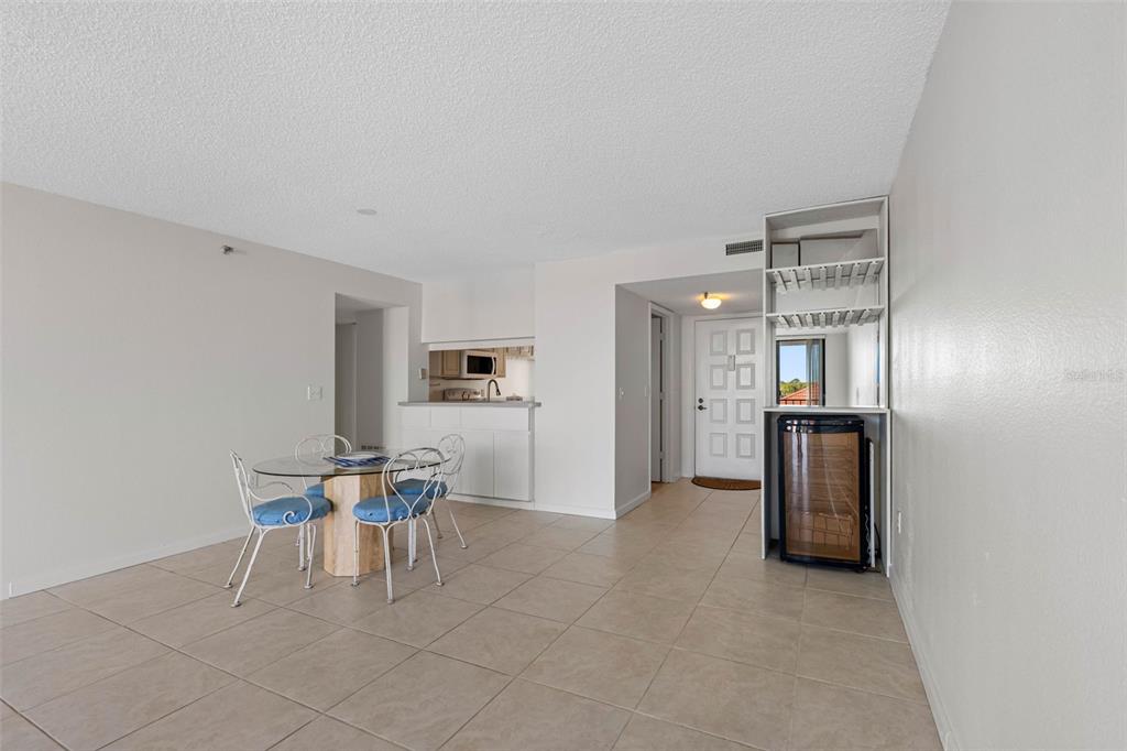 A dining area with a glass table, blue chairs, tile floors, and a wine cooler — 19111 VISTA BAY DRIVE UNIT 204, INDIAN SHORES, FL