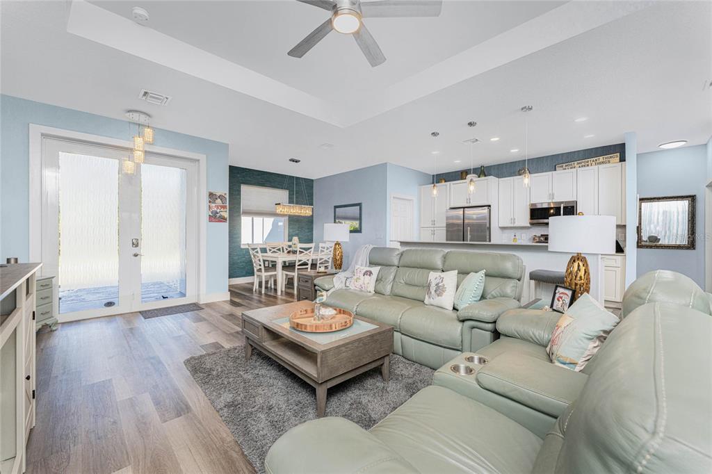 An open-concept living room and kitchen featuring light blue walls, wood-look flooring, and a sectional sofa — 23387 CEDARTON AVENUE, PUNTA GORDA, FL