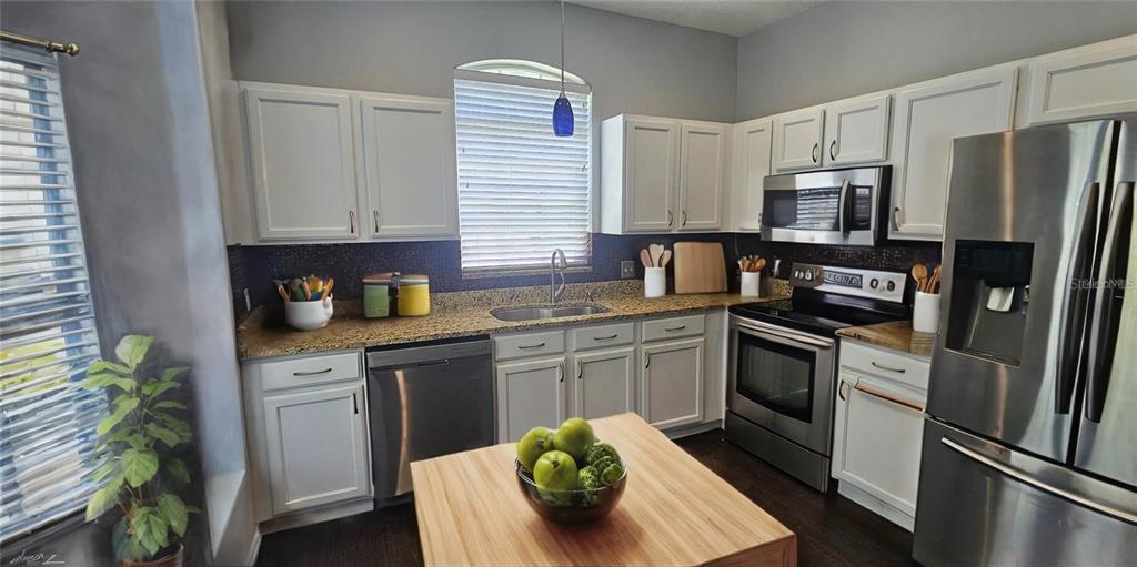 A kitchen features white cabinets, granite countertops, stainless steel appliances, and a wooden island — 4337 DEERMONT CIRCLE, TAMPA, FL