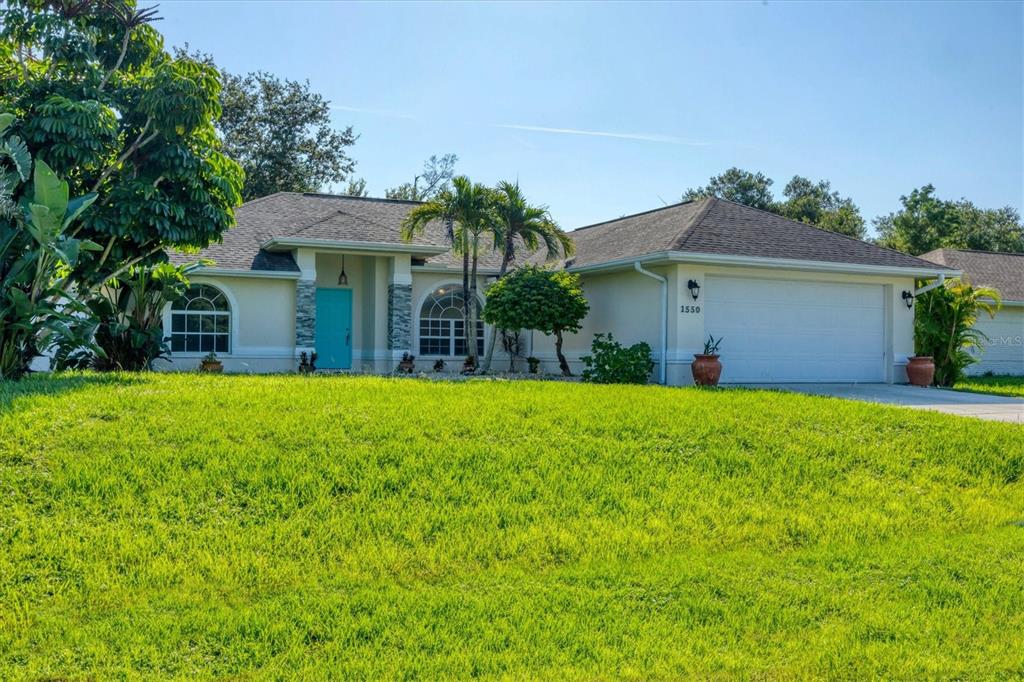 A single-story house with a turquoise front door, a two-car garage, and a grassy lawn — 1550 S BISCAYNE DRIVE, NORTH PORT, FL