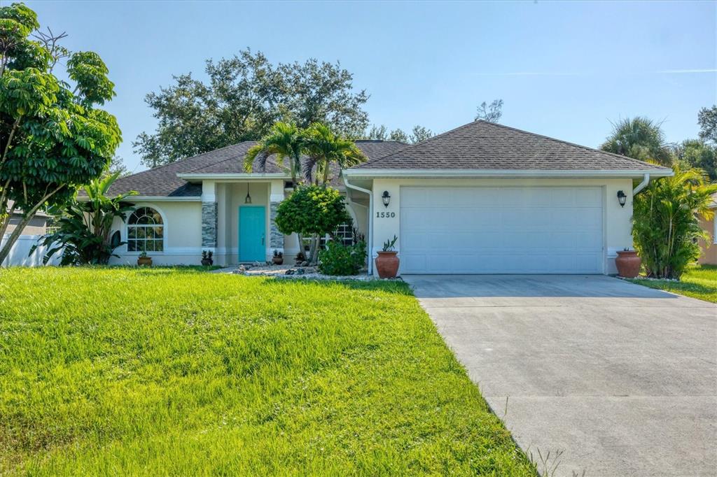 A single-story house with a turquoise front door, a two-car garage, and a grassy lawn — 1550 S BISCAYNE DRIVE, NORTH PORT, FL