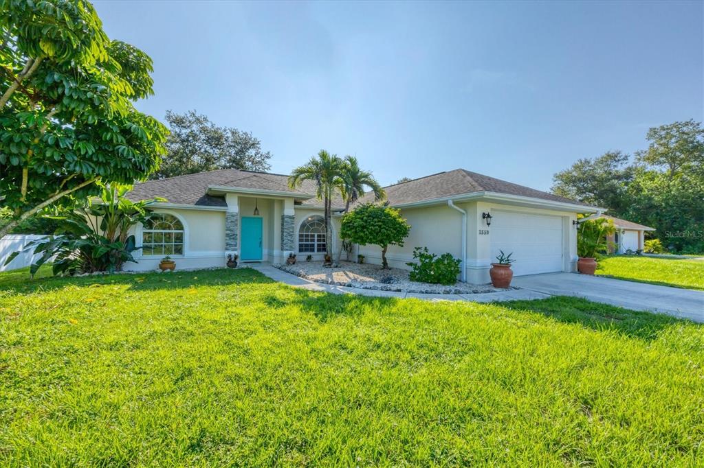 A single-story house with a light-colored exterior, a blue front door, and a two-car garage — 1550 S BISCAYNE DRIVE, NORTH PORT, FL