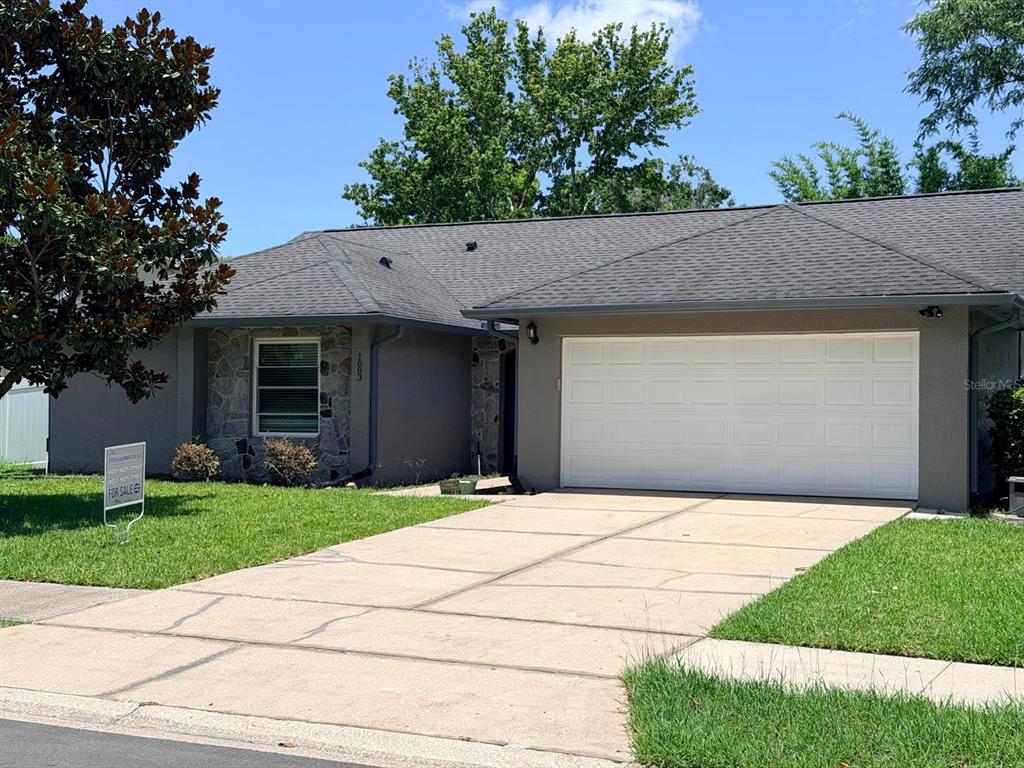 A single-story house with a gray exterior, stone accents, a two-car garage, and a driveway — 1083 BECKSTROM DR, OVIEDO, FL