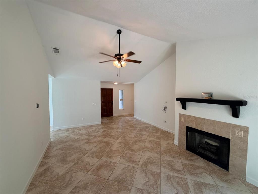 A living room with vaulted ceilings, tile flooring, and a fireplace with a black mantel — 1083 BECKSTROM DR, OVIEDO, FL