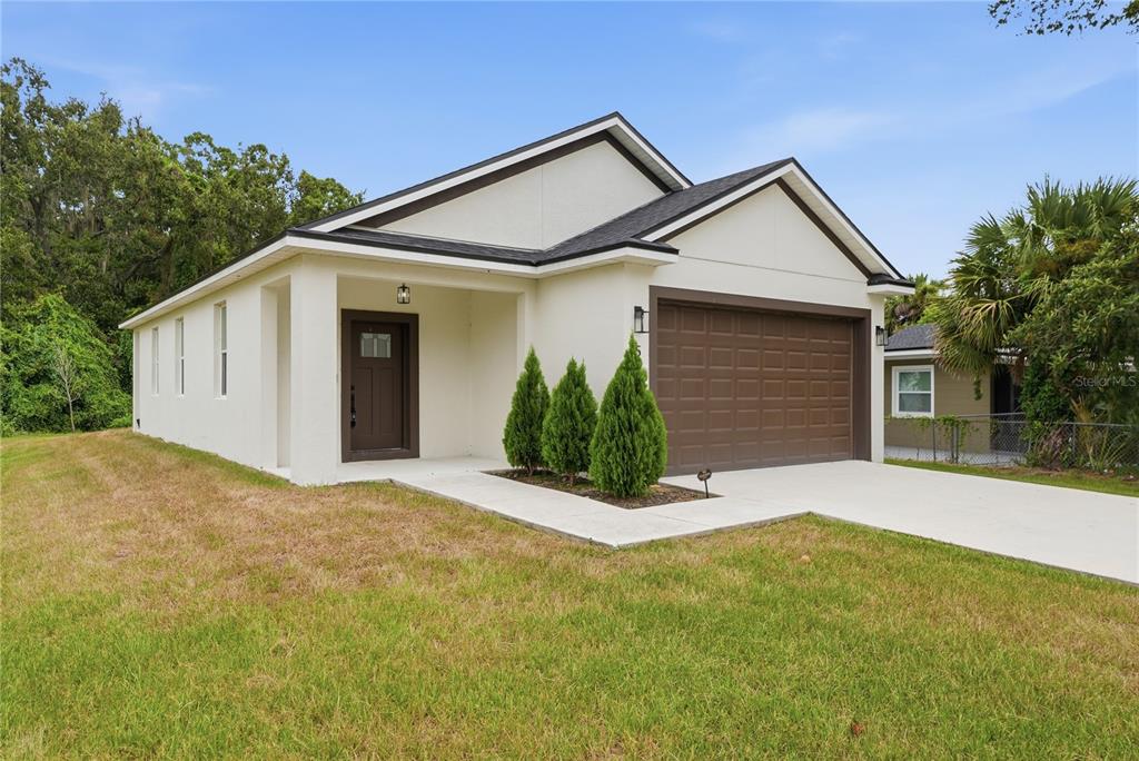 A single-story house with a white stucco exterior, brown garage door, and three small evergreen trees — 5401 OLD CHENEY HIGHWAY, ORLANDO, FL