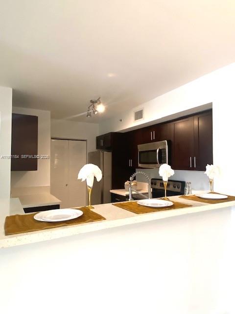 A kitchen features dark wood cabinets, stainless steel appliances, and a breakfast bar with place settings — 2061 Renaissance Blvd # 204, Miramar FL 33025, MIRAMAR, FL