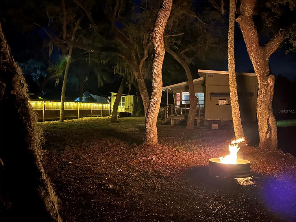 A backyard at night features a fire pit, mature trees, and a small mobile home — 14272 W SUTTON COURT, CRYSTAL RIVER, FL