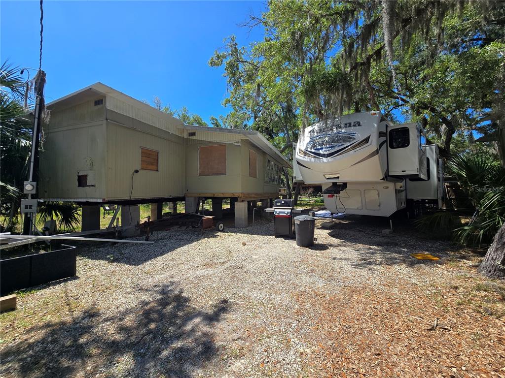 An elevated mobile home sits next to a parked fifth-wheel RV on a gravel lot — 14272 W SUTTON COURT, CRYSTAL RIVER, FL