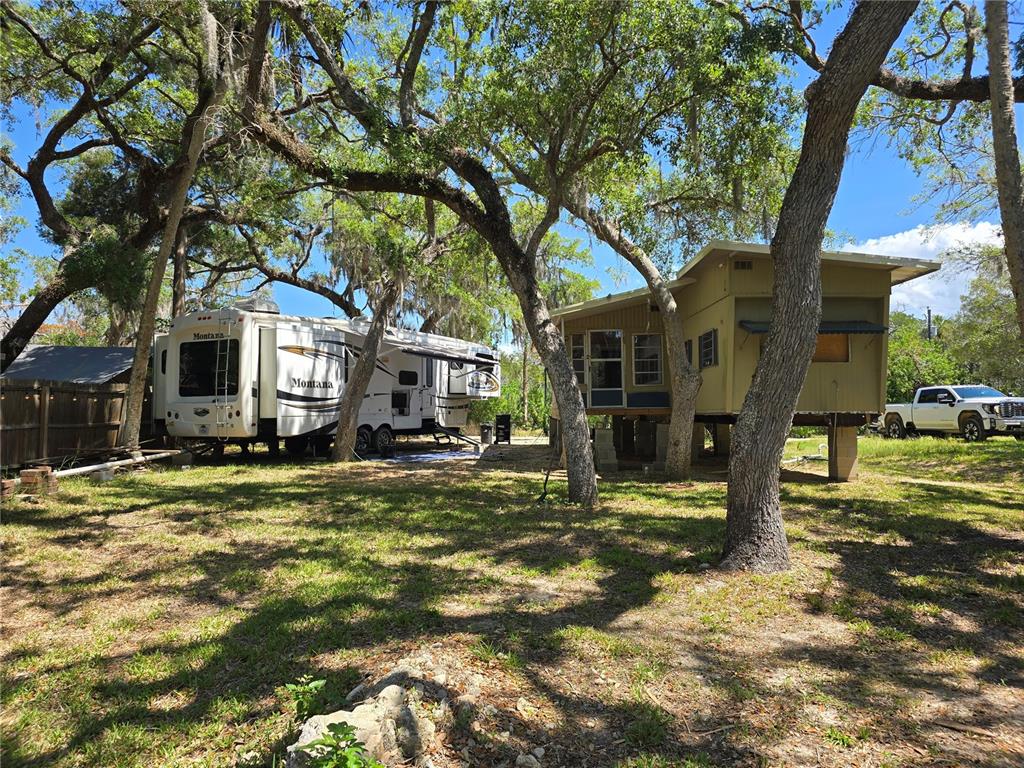 A white Montana fifth-wheel trailer and a tan elevated mobile home sit under large trees — 14272 W SUTTON COURT, CRYSTAL RIVER, FL