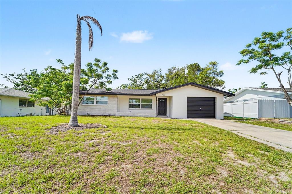 A single-story house with a white exterior, dark garage door, and a front yard — 7808 BRACKEN DRIVE, PORT RICHEY, FL