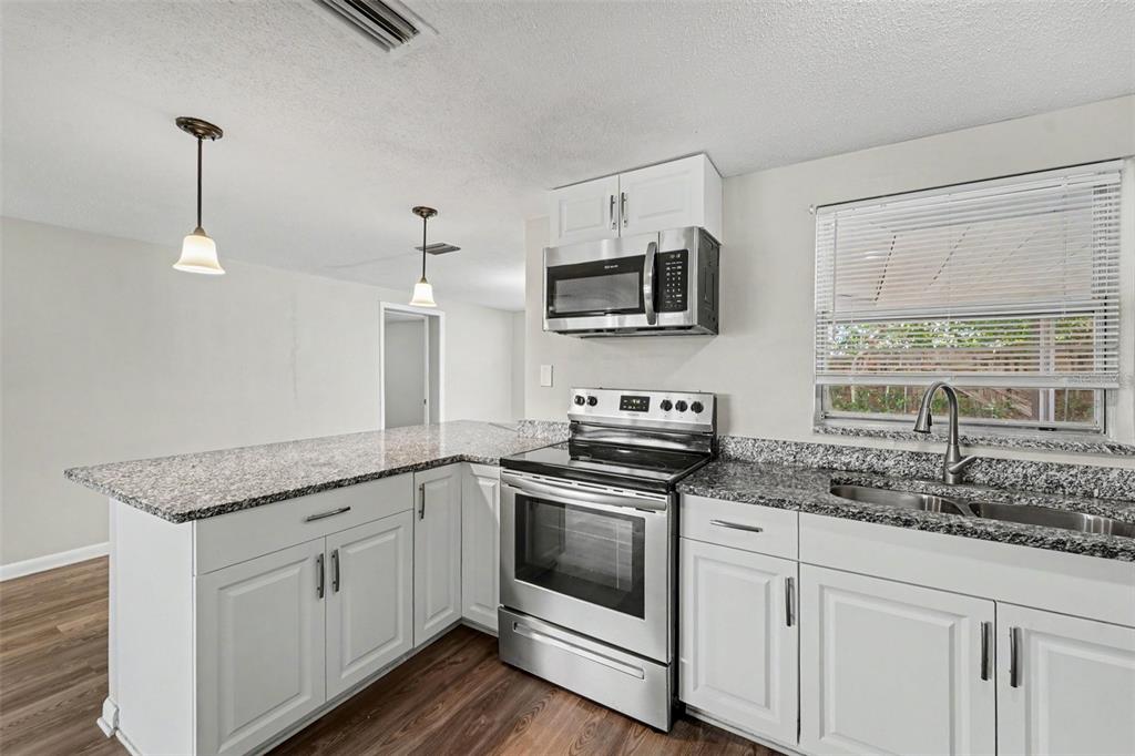 A kitchen features white cabinets, granite countertops, stainless steel appliances, and wood-look flooring — 7808 BRACKEN DRIVE, PORT RICHEY, FL