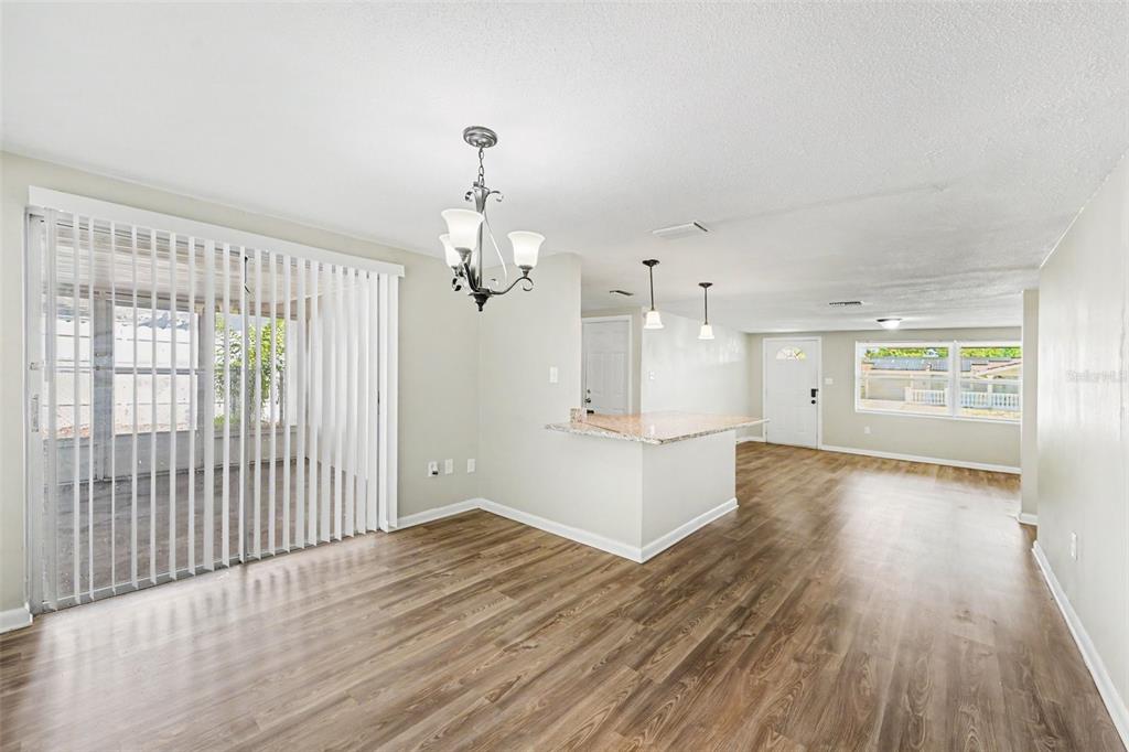 An open-concept living and dining area features wood-look flooring, a kitchen island, and sliding doors — 7808 BRACKEN DRIVE, PORT RICHEY, FL