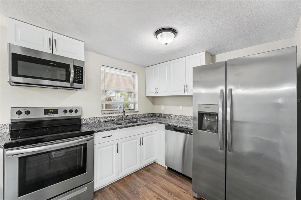 A kitchen with white cabinets, stainless steel appliances, and dark granite countertops — 7808 BRACKEN DRIVE, PORT RICHEY, FL