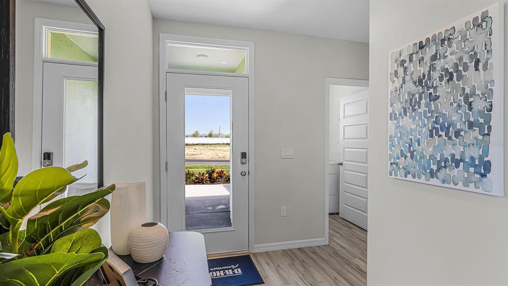 An entryway features a glass-paneled front door, light wood flooring, and a blue abstract painting — 4052 GIORGIO DRIVE, WINTER HAVEN, FL