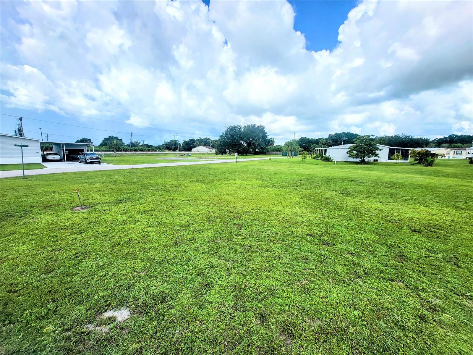 A large, grassy vacant lot is situated between two residential buildings under a cloudy sky — 803 & 805 & 805 Big Branch Lane, Moore Haven FL 33471, MOORE HAVEN, FL