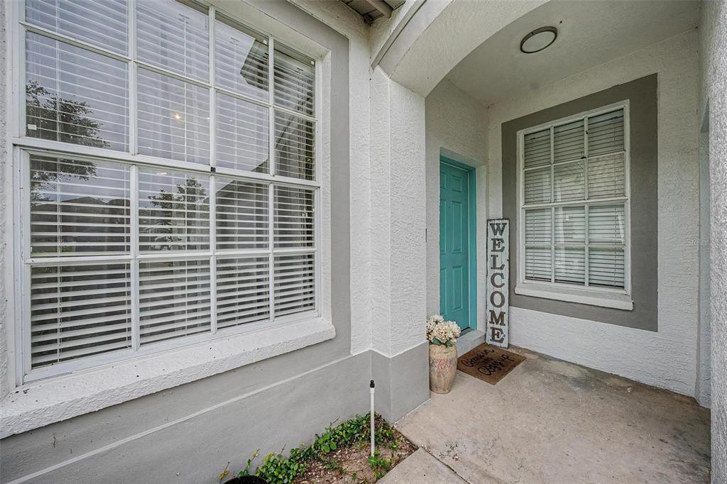 A front porch features a teal door, a welcome sign, and two windows with blinds — 19309 WEYMOUTH DRIVE, LAND O LAKES, FL