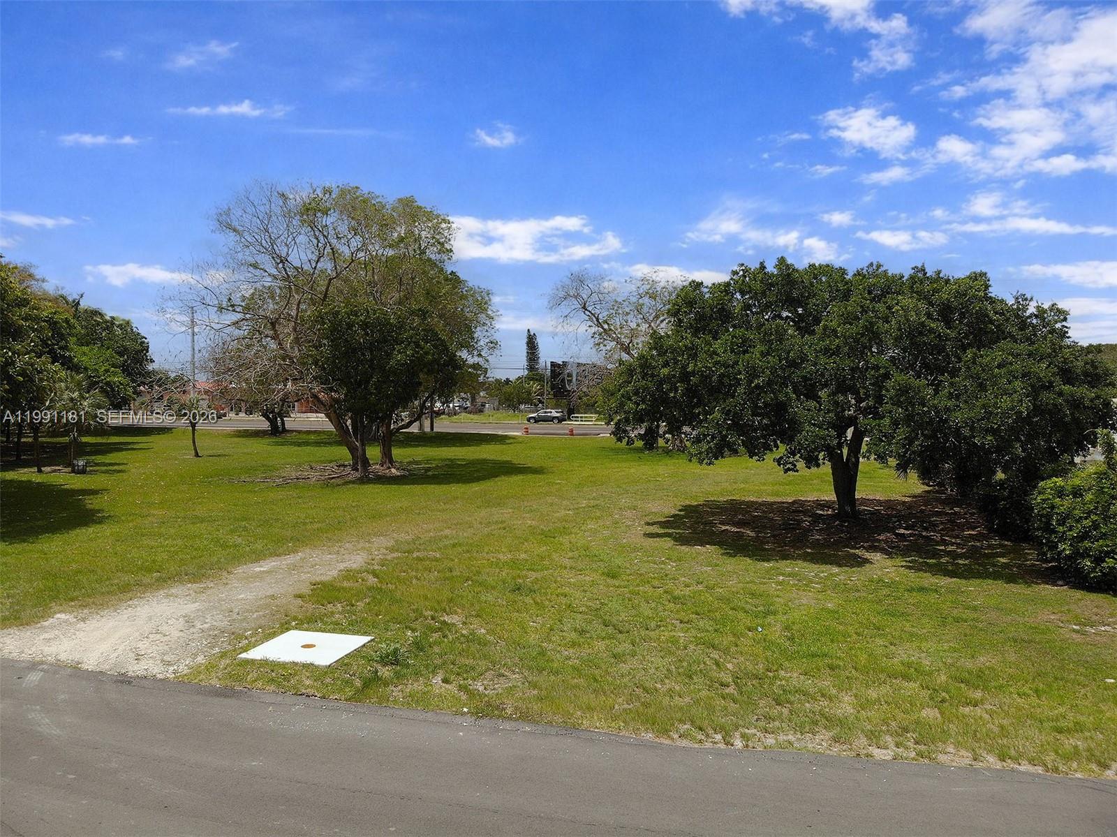 A grassy, open lot features several large trees under a bright, partly cloudy blue sky — 22650 SW 123rd Rd, Miami FL 33170, MIAMI, FL
