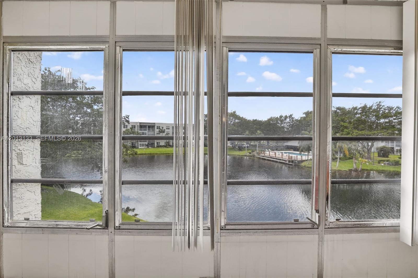 A view of a lake and pool area through a multi-pane window with vertical blinds — 9330 Lagoon Pl # 307, Davie FL 33324, DAVIE, FL