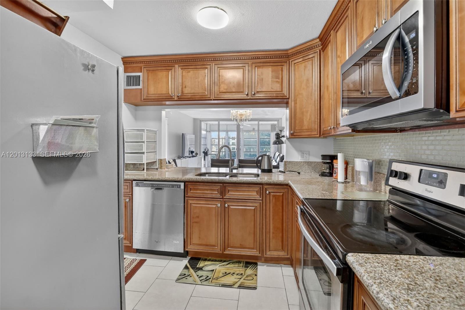 A kitchen features wood cabinets, stainless steel appliances, granite countertops, and a pass-through window — 9330 Lagoon Pl # 307, Davie FL 33324, DAVIE, FL