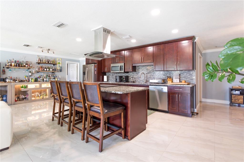 A kitchen features dark wood cabinetry, granite countertops, a center island, and a home bar — 2198 OAK GROVE DRIVE, CLEARWATER, FL