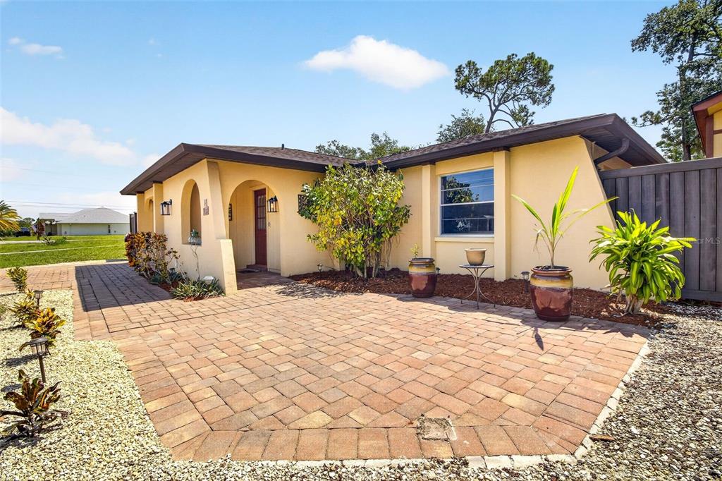 A yellow house exterior features a brick paver patio, arched entryway, and a wooden fence — 1018 KENSINGTON STREET, PORT CHARLOTTE, FL