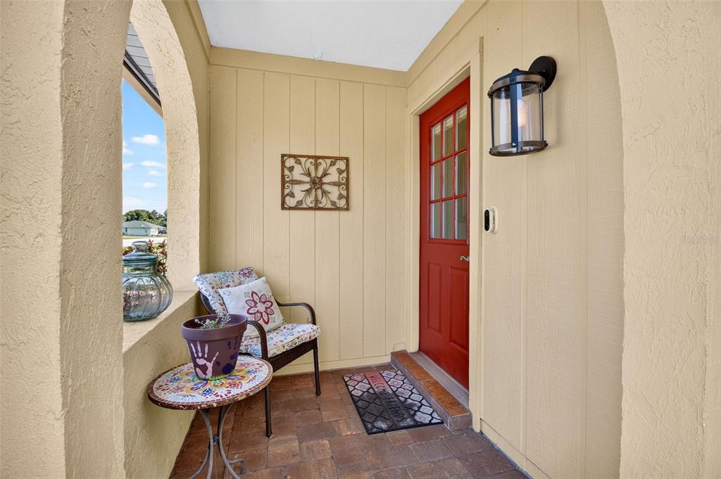 A covered front porch features a red door, a small bistro table, and a chair — 1018 KENSINGTON STREET, PORT CHARLOTTE, FL