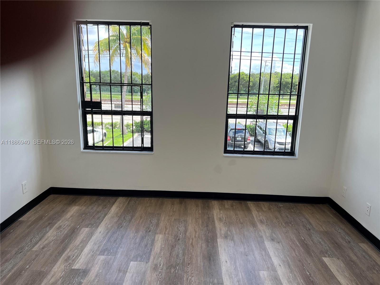 An empty room with wood-look flooring, white walls, black baseboards, and two barred windows — 2001 N Dixie Hwy, Pompano Beach FL 33060, POMPANO BEACH, FL
