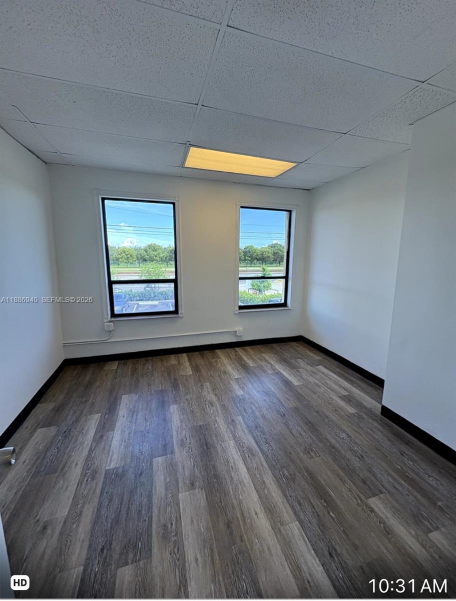An empty office room features white walls, wood-look flooring, two windows, and a drop ceiling — 2001 N Dixie Hwy, Pompano Beach FL 33060, POMPANO BEACH, FL