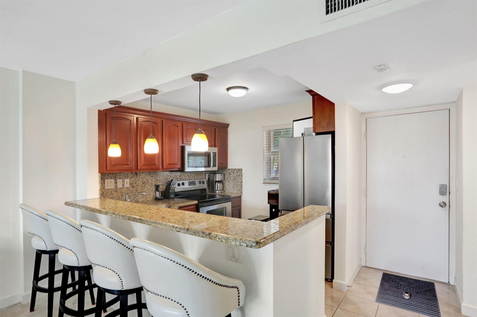 A kitchen with granite countertops, wooden cabinets, stainless steel appliances, and a breakfast bar — 1391 S Ocean Boulevard # 206, Pompano Beach FL 33062, POMPANO BEACH, FL