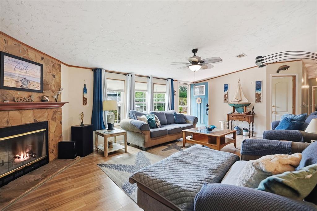 A living room features a stone fireplace, wood-look flooring, a ceiling fan, and blue furniture — 825 N GRIFFITH AVENUE, CRYSTAL RIVER, FL