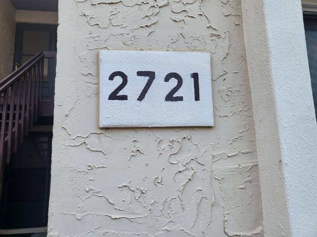 A white rectangular plaque with the black numbers 2721 is mounted on a textured stucco wall — 2721 HIDDEN LAKE BOULEVARD UNIT C, SARASOTA, FL