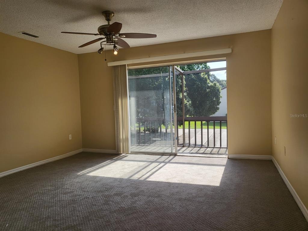 A carpeted room with a ceiling fan and sliding glass doors leading to a balcony — 2721 HIDDEN LAKE BOULEVARD UNIT C, SARASOTA, FL