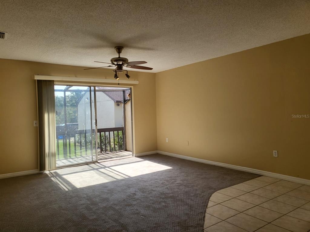 A living room features beige walls, gray carpeting, a ceiling fan, and sliding glass balcony doors — 2721 HIDDEN LAKE BOULEVARD UNIT C, SARASOTA, FL