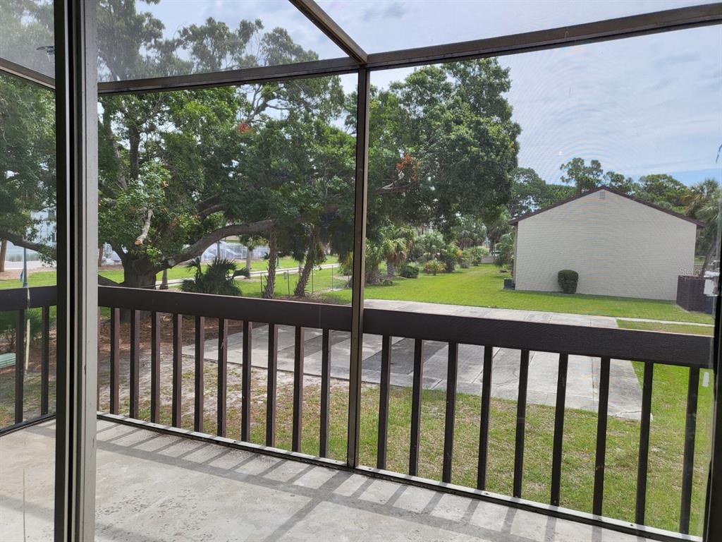 A screened-in balcony overlooks a grassy yard, a parking area, and mature trees — 2721 HIDDEN LAKE BOULEVARD UNIT C, SARASOTA, FL