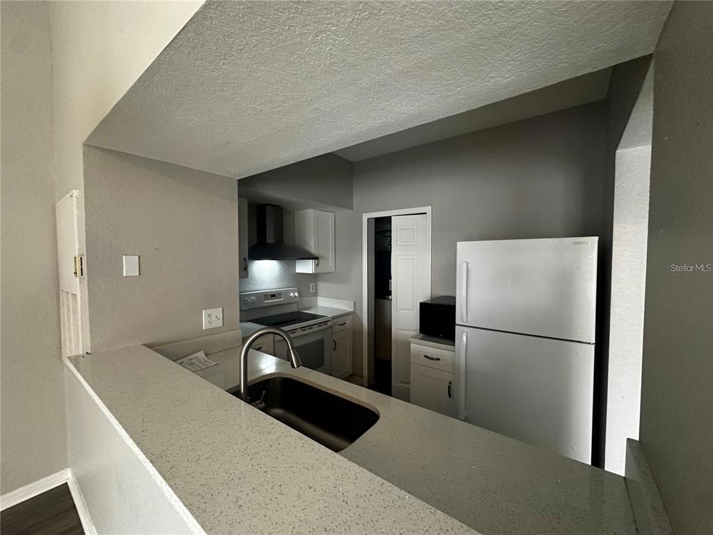 A kitchen features a breakfast bar, stainless steel sink, white appliances, and gray walls — 2314 MIDTOWN TERRACE UNIT 1125, ORLANDO, FL