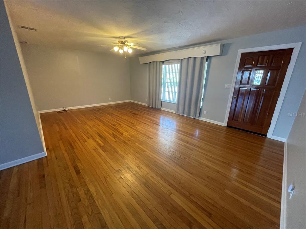 An empty living room features hardwood floors, light gray walls, and a wooden front door — 6219 12TH AVENUE S, GULFPORT, FL