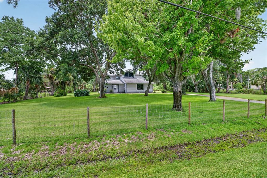 A two-story house with light siding sits on a large lawn behind a wire fence — 3247 DALHI STREET, COCOA, FL