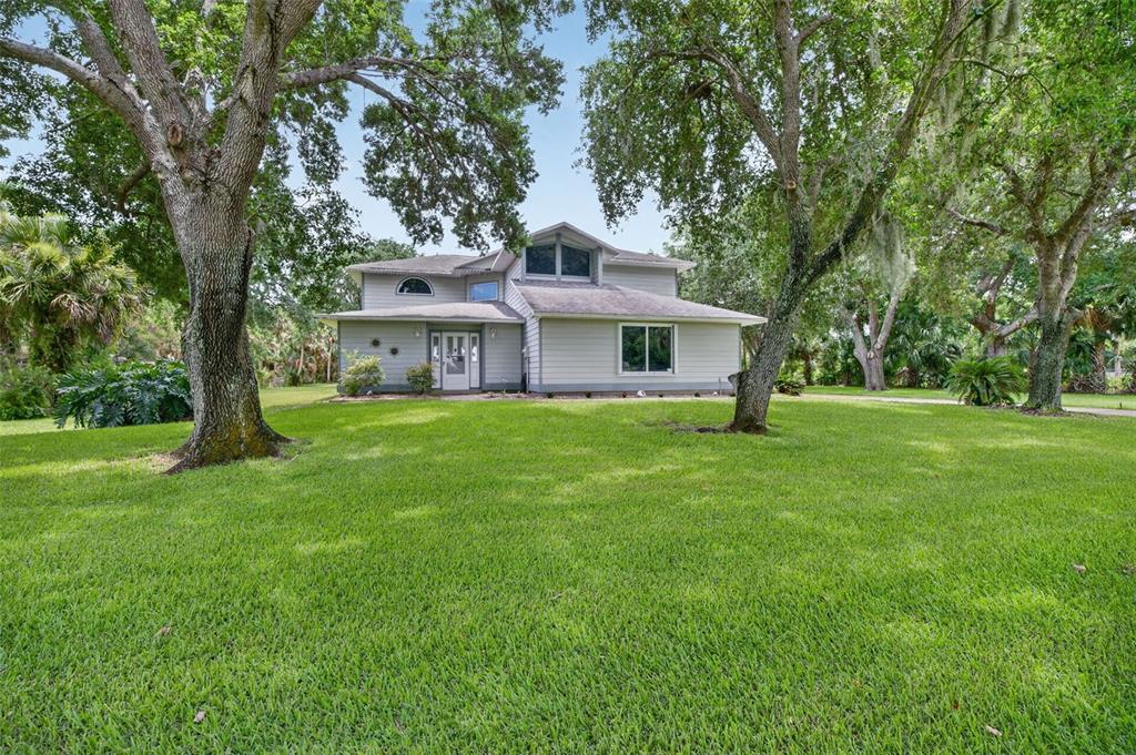 A two-story house with light gray siding sits on a large, tree-shaded grassy lawn — 3247 DALHI STREET, COCOA, FL