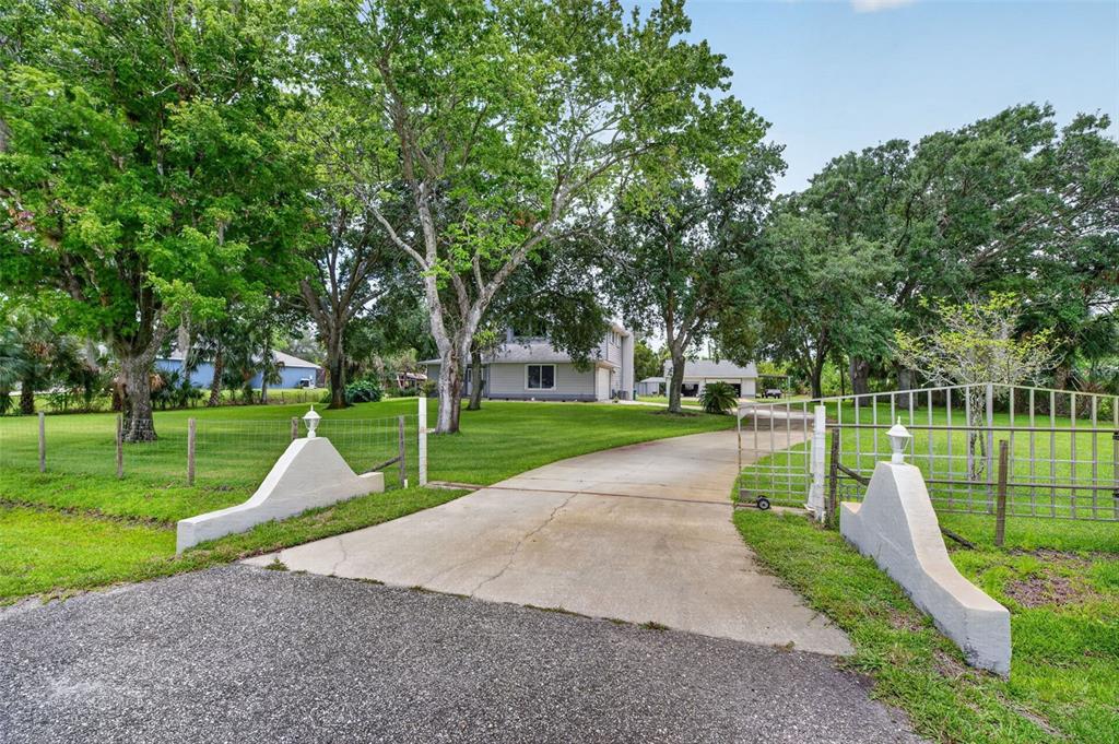 A concrete driveway leads through a gated entrance toward a house surrounded by large trees — 3247 DALHI STREET, COCOA, FL