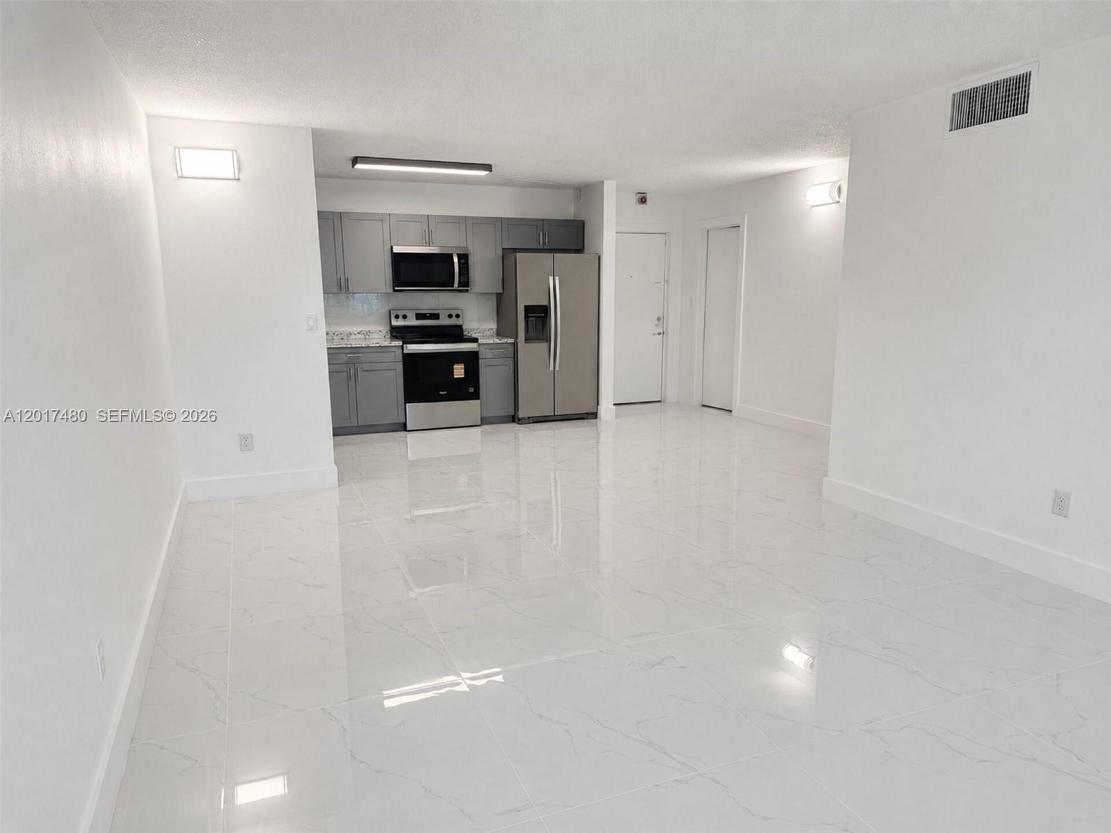A kitchen with gray cabinets and stainless steel appliances opens into a white-tiled living area — 14830 Naranja Lakes Blvd, Homestead FL 33032, HOMESTEAD, FL