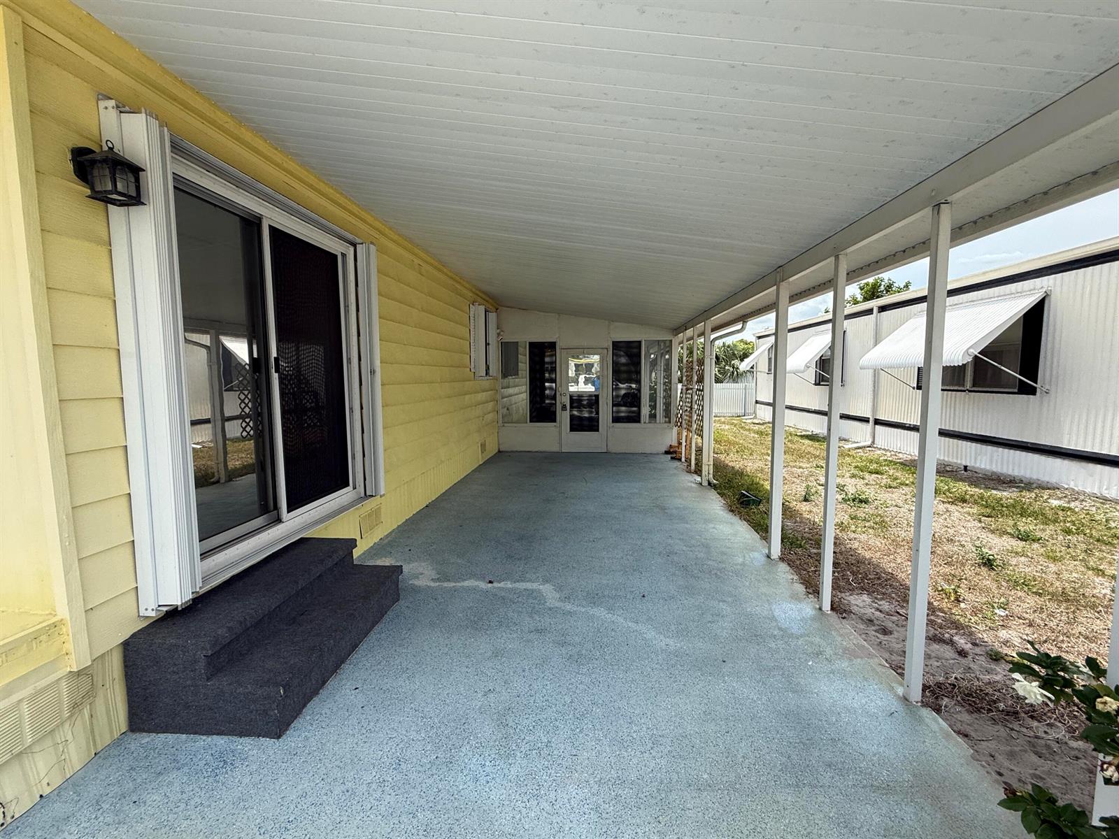 A covered concrete patio runs alongside a yellow mobile home with a sliding glass door — 7089 SE Bluebird Circle, Hobe Sound FL 33455, HOBE SOUND, FL