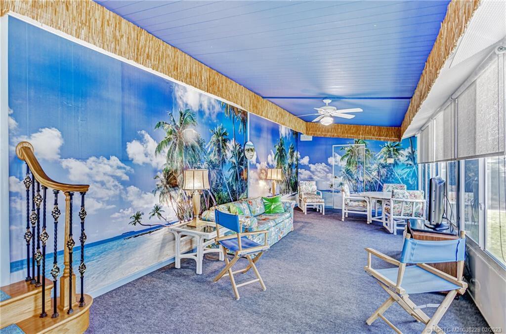 A sunroom features a tropical mural wall, blue ceiling, and a staircase with wooden railings — 7089 SE Bluebird Circle, Hobe Sound FL 33455, HOBE SOUND, FL