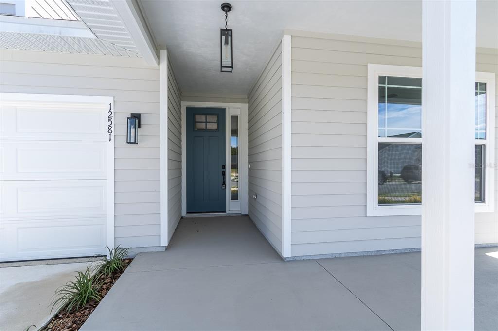 A covered front porch features a blue door, light gray siding, and a concrete floor — 12581 NW 159TH WAY, ALACHUA, FL