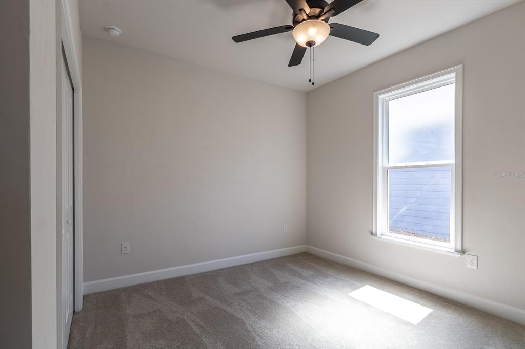 A small bedroom with beige walls, carpeted flooring, a ceiling fan, and a single window — 12581 NW 159TH WAY, ALACHUA, FL