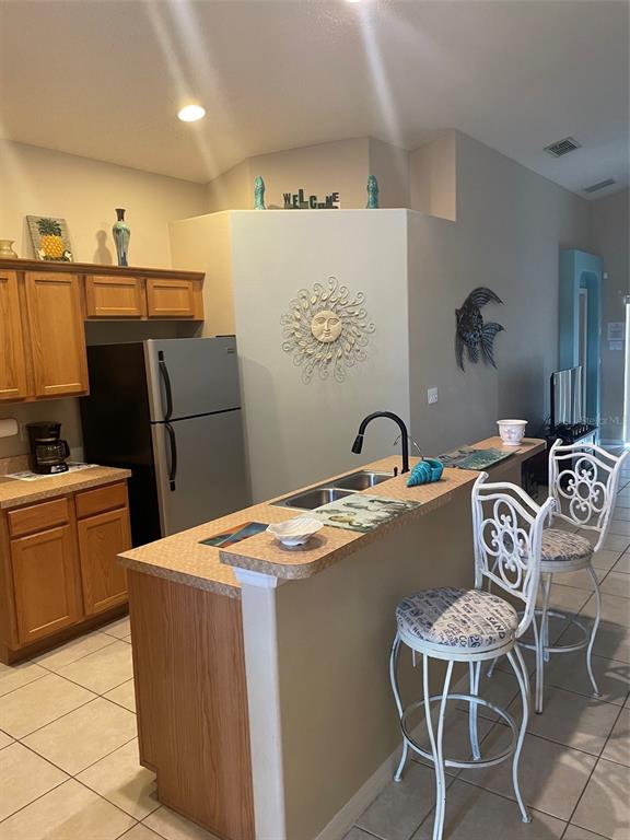 A kitchen features light wood cabinets, a breakfast bar with two stools, and tile flooring — 16705 FRESH MEADOW DRIVE, CLERMONT, FL